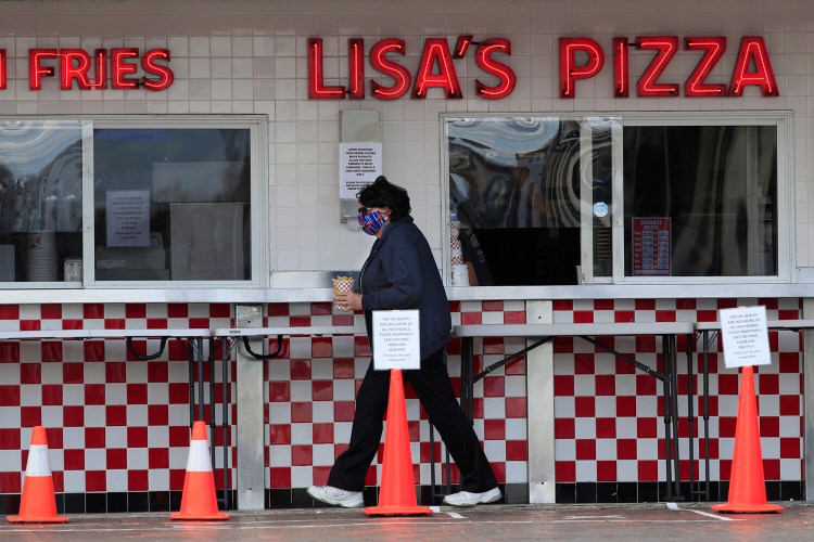 A customer leaves the sidewalk window with her French fries at Lisa's Pizza in Old Orchard Beach on Thursday. The business is one of the few in the tourist town that have reopened during the coronavirus pandemic.