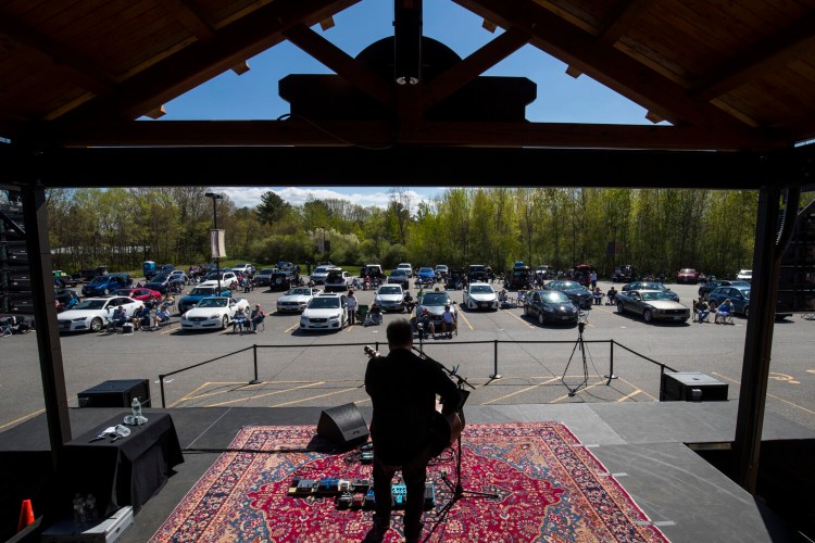 People sit by their cars as they watch Tim Theriault perform at Tupelo Music Hall in Derry, N.H., on Saturday, in the first drive-in concert there since the outbreak. 