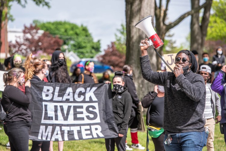 Dane Morgan speaks through a megaphone while others hold a Black Lives Matter sign during a rally on June 1, 2020, in Kennedy Park in Lewiston.