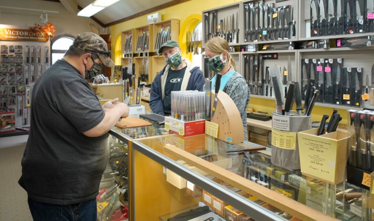 James Conner, left, looks over a knife while talking with Doug Dillman, center, and Jason Dillman of Casco Bay Cutlery & Kitchenware in Freeport on Monday, the first day nonessential retail businesses could open in southern Maine.