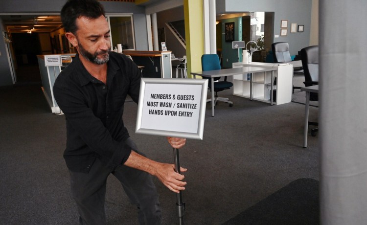 Patrick Roche of Think Tank Coworking puts a sign near the entrance to remind members and guests to sanitize hands Thursday in Portland. Startup companies, and businesses that cater to them such as Think Tank, have undergone dramatic changes because of the pandemic.