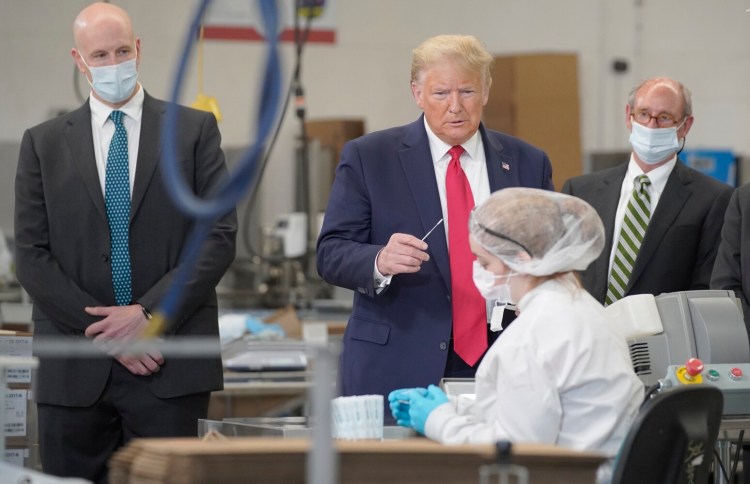 President Donald Trump holds a swab while speaking Friday with an employee of Puritan Medical Products during a tour of the factory in Guilford, which makes the swabs used in COVID-19 testing. 