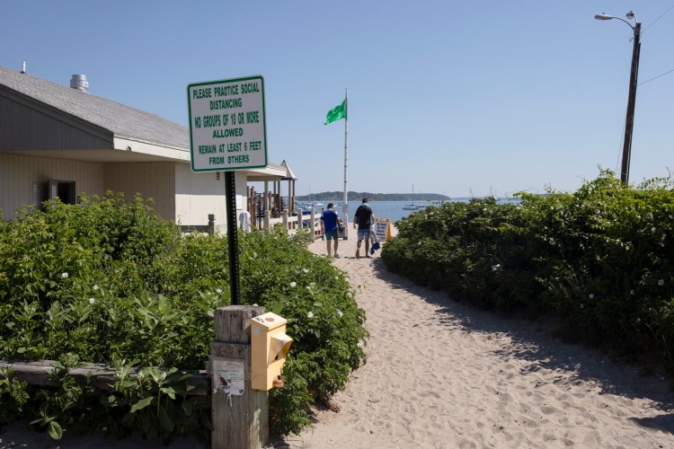 A sign asking beachgoers to maintain social distance sits at the entrance to Willard Beach in South Portland on Saturday.