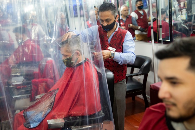 Peter Shamuelov, center, wears a protective mask as he gives a haircut to a customer at Ace of Cuts barbershop on Monday in New York. For the first time in three months, New Yorkers are able to dine out, browse the city's destination stores and get haircuts. 