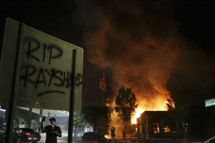 "RIP Rayshard" is spray painted on a sign as as flames engulf a Wendy's restaurant during protests Saturday in Atlanta. The restaurant was where Rayshard Brooks was shot and killed by police Friday evening following a struggle in the restaurant's drive-thru line.