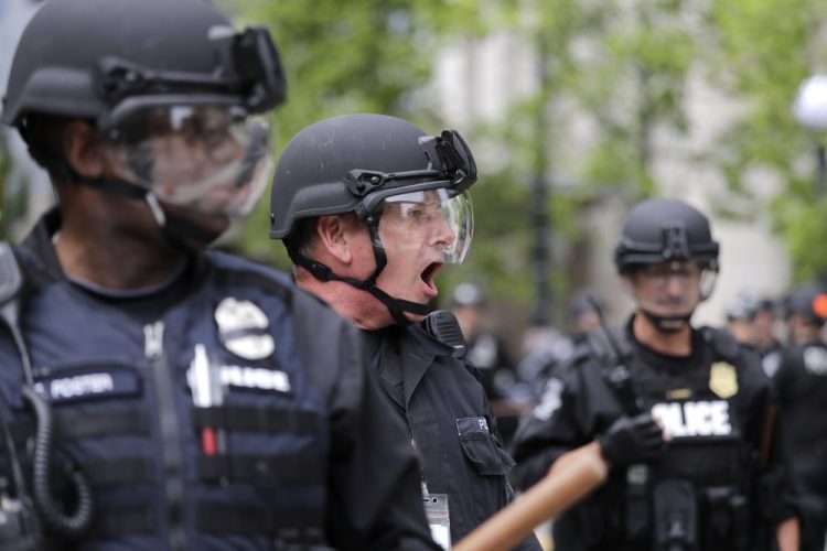 A Seattle police officer yells out orders at Seattle City Hall as protesters march toward them Wednesday, June 3, 2020, protesting the death of George Floyd in Minneapolis.