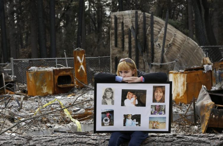 Christina Taft, the daughter of Camp Fire victim Victoria Taft, displays a collage of photos of her mother, at the burned out ruins of the Paradise, Calif., home where she died in 2018. Pacific Gas & Electric plead guilty for the deadly wildfire that nearly wiped out the Northern California town of Paradise in 2018. 
