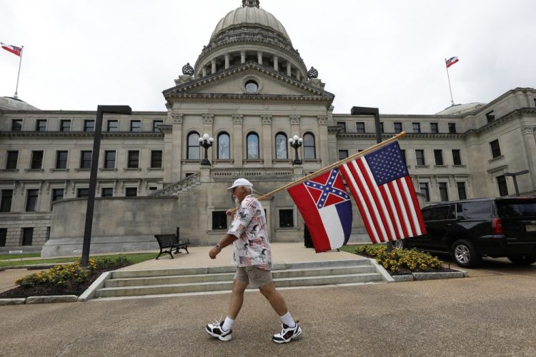 Don Hartness of Ellisville, walks around the Capitol carrying the current Mississippi state flag and the American flag on Saturday in Jackson, Miss. 

