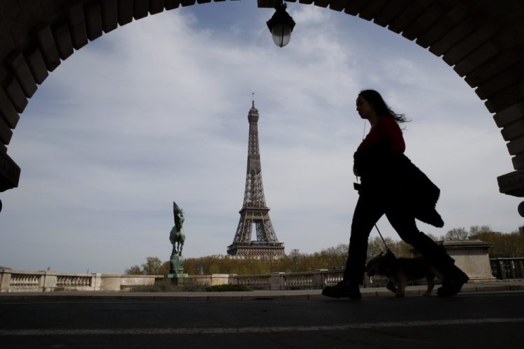 A woman walks her dog on a Paris bridge, with the Eiffel tower in background, in April during a nationwide confinement to counter the COVID-19. The European Union announced Tuesday that it will reopen its borders to travelers from 14 countries, but most Americans have been refused entry for at least another two weeks due to soaring coronavirus infections in the U.S. 