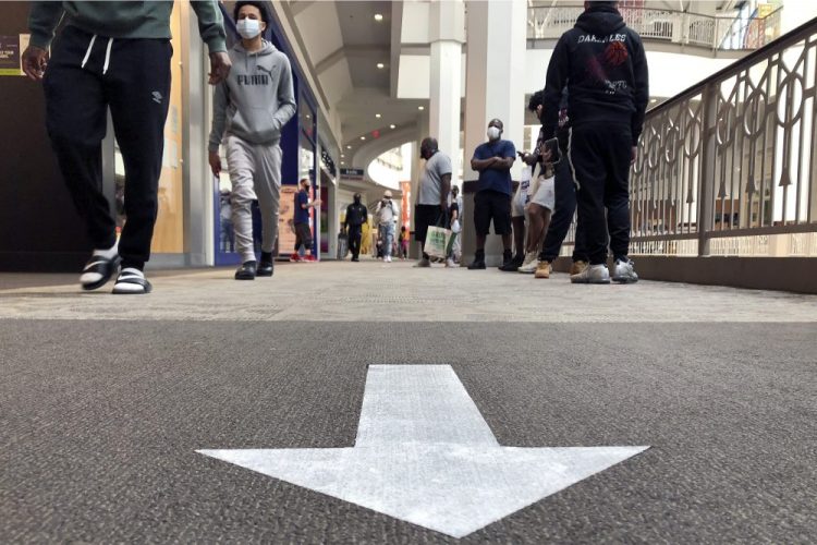 Shoppers walk near a social distancing arrow on a carpet in a hallway at Providence Place shopping mall in June in Providence, R.I. The mall has taken safety measures in response to the pandemic, including safe-distancing signage and hand-sanitizing stations in common areas.