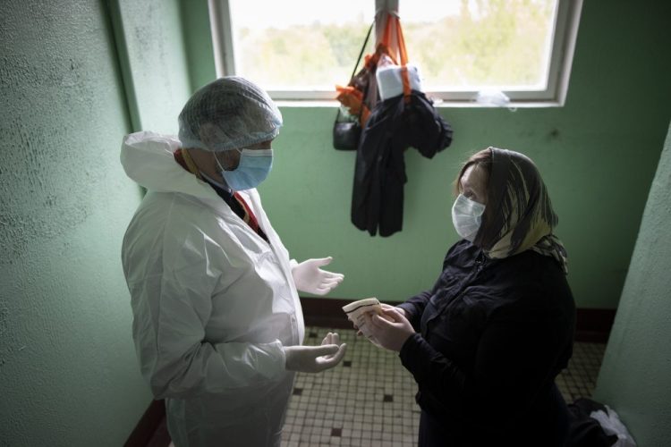 In this photo taken on Tuesday, May 26, 2020, a volunteer helps Father Vasily Gelevan put on a biohazard suit and gloves to protect against the coronavirus before visiting a patient suspected of being infected with COVID-19 at her apartment in Moscow, Russia. In addition to his regular duties as a Russian Orthodox priest, Father Vasily visits people infected with COVID-19 at their homes and hospitals. 