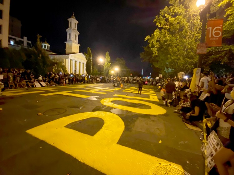 People gather along a street painted with "Defund the police" near the White House on Saturday night. 