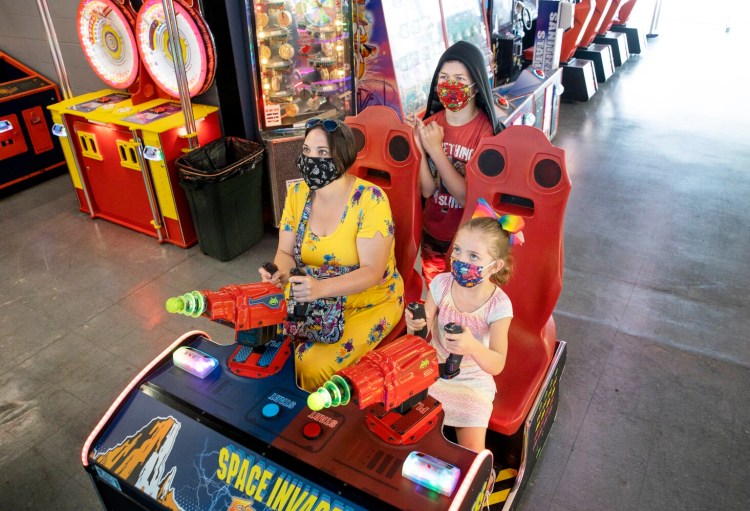 Sarah Luna of Ellsworth plays an arcade game with her daughter Fable, 6, while her stepson Trey Roehrich, 13, looks on at Palace Playland in Old Orchard Beach on Wednesday. Maine businesses such as arcades, movie theaters, bowling alleys and amusement parks were allowed to reopen to the public Wednesday with strict occupancy limits.