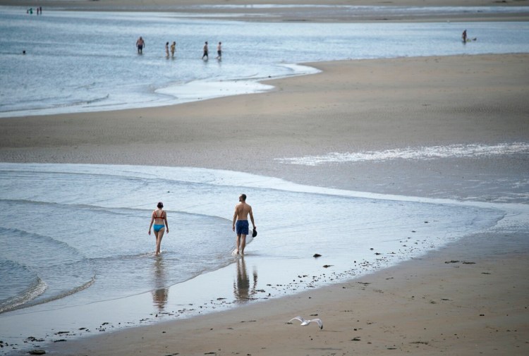 People walk in the shallow water on Thursday at Popham Beach State Park, where bathers were told to only go in the water ankle deep that day because of a recent shark attack and subsequent shark sightings off the Maine coast. 
