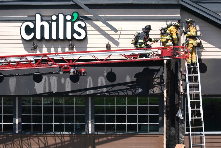 Firefighters work to pull charred pieces of siding and wood from the Chili’s restaurant near The Maine Mall in South Portland on Monday. Officials don’t yet know the cause of the fire, which they said was brought under control in about 10 minutes. 