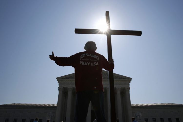 A man holds a cross as he prays prior to rulings on religious school issues outside the Supreme Court in Washington on July 8, 2020. AP Photo/Patrick Semansky