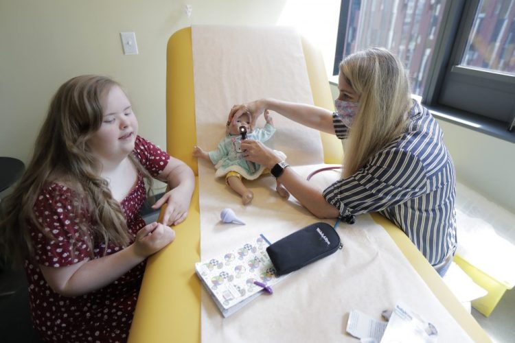 Emilyanne Wade, 12, left, looks on as Tricia Nora, a pediatric nurse practitioner, examines Sophia, Wade's baby doll in a medical clinic at Mary's Place, a family homeless shelter located inside an Amazon corporate building on the tech giant's Seattle campus.