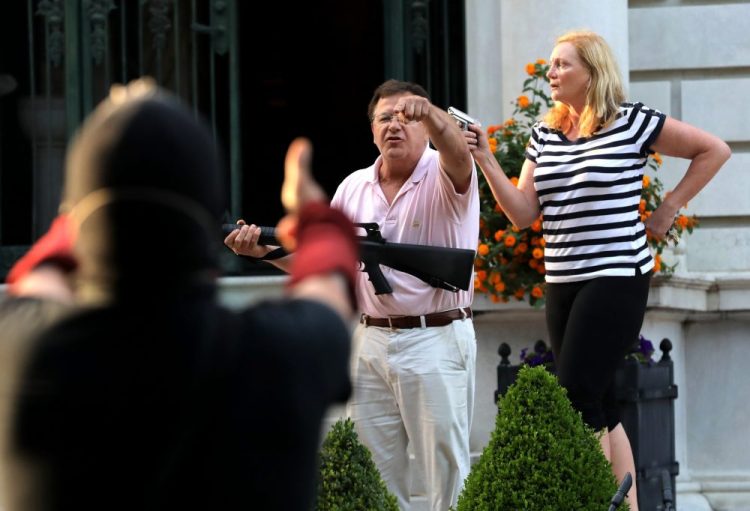 Armed homeowners Mark and Patricia McCloskey, standing in front their house, confront protesters marching to St. Louis Mayor Lyda Krewson's house in the Central West End of St. Louis on June 28. St. Louis’ top prosecutor said Monday she is charging the couple with felony unlawful use of a weapon. 