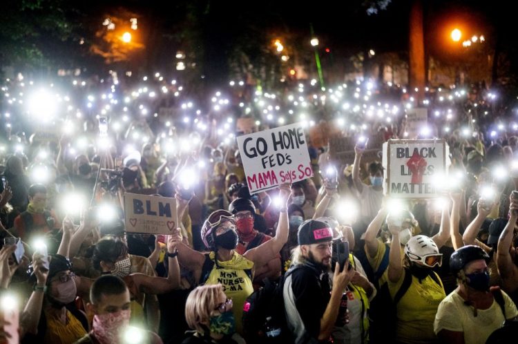 Hundreds of Black Lives Matter protesters hold their phones aloft on Monday in Portland, Ore. Federal officers’ actions at protests in Oregon’s largest city, hailed by President Trump but done without local consent, are raising the prospect of a constitutional crisis – one that could escalate as weeks of demonstrations find renewed focus in clashes with camouflaged, unidentified agents outside Portland’s U.S. courthouse. 