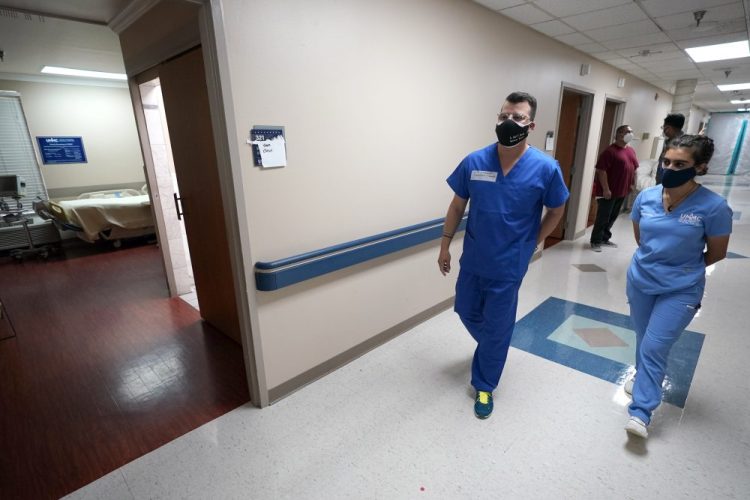 Infectious disease physician Army Maj. Gadiel Alvarado, left, with the Urban Augmentation Medical Task Force, walks down the hall with United Memorial Medical Center's Mariya Mohiuddin, director of COVID-19 testing and logistics, inside a newly set up wing in the hospital in Houston on Thursday. Texas reported a new daily record for virus deaths Friday and more than 10,000 confirmed cases for the fourth consecutive day.