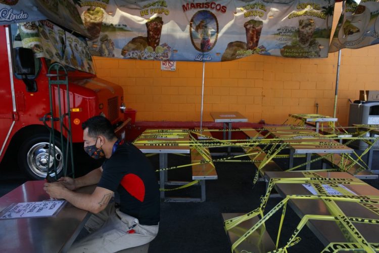 Abel Gomez waits for his order at Mariscos Linda food truck on July 1 as dining tables are sealed off with caution tape due to the coronavirus pandemic in Los Angeles. California Gov. Gavin Newsom extended the closure of bars and indoor dining statewide and has ordered gyms, churches and hair salons closed in most places as coronavirus cases keep rising.