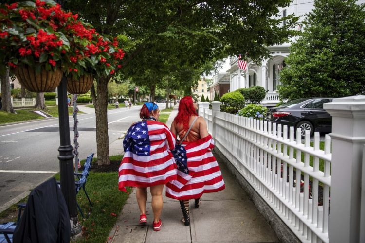 Parade goers draped in American flags walk down the street before a Fourth of July parade begins Saturday in Bristol, R.I. The town, which lays claim to the nation's oldest Independence Day celebration in the country, held a vehicle-only scaled down version of its annual parade Saturday due to the coronavirus pandemic.
