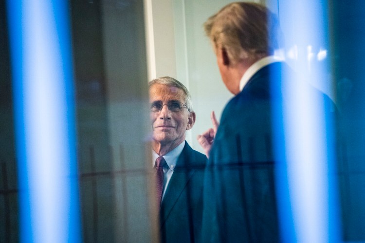 Pictured through a windown, Anthony Fauci, left, and President Trump talk during an April task force briefing on the coronavirus. But Fauci has not spoke with Trump since the first week of June and the White House has limited his appearances in the media.