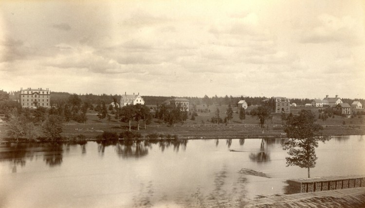 An image scanned from a black and white photograph with the caption, "Maine State College, looking North from Orono." Buildings visible include Oak Hall on the left, White Hall (later renamed Wingate and replaced with the modern Wingate when this wooden structure burned in 1890), Fernald Hall, Coburn Hall, and agricultural buildings. Stacks of sawed lumber appear in the foreground, on the Orono side of the Stillwater River.

Image courtesy of Special Collections, Raymond H. Fogler Library, DigitalCommons@UMaine

MeBi