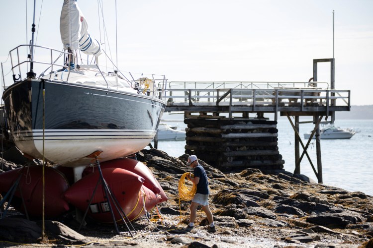 Henry Norris works to stabilize a sailboat that washed ashore in Falmouth overnight as the remnants of Hurricane Isaias blew through Maine. Norris was working with Determination Marine, a company that specializes in salvaging boats, and planned to float the boat back out at high tide on Wednesday. 
