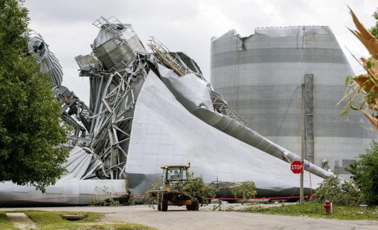 Iowa Department of Transportation workers help with tree debris removal as grain bins from the Archer Daniels Midland facility are seen severely damaged in Keystone, Iowa, on Wednesday. A storm slammed the Midwest with straight line winds of up to 100 miles per hour on Monday, gaining strength as it plowed through Iowa farm fields, flattening corn and bursting grain bins still filled with tens of millions of bushels of last year’s harvest.
