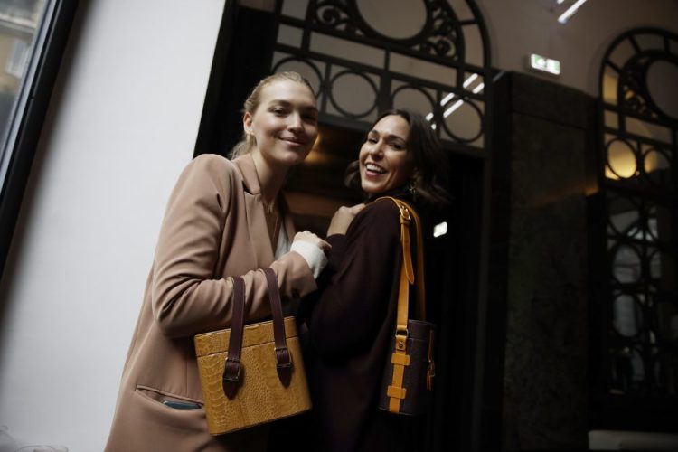 Model Arizona Muse, left, and designer and Officina del Poggio owner Allison Hoeltzel Savini  present a creation of the Officina del Poggio women's Fall-Winter 2019-2020 collection, in Milan, Italy, last year.  Officina del Poggio sells 60 percent of its vintage motorcycle-inspired satchels to U.S. customers, and the economic slowdown has Hoeltzel Savini worried for next year. 