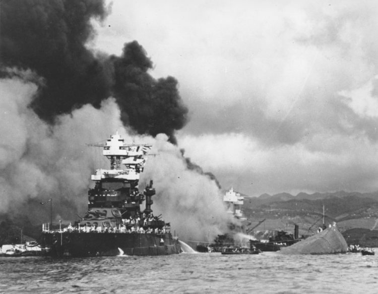 Part of the hull of the capsized USS Oklahoma is seen at right as the battleship USS West Virginia, center, begins to sink after the Dec. 7, 1941, attack on Pearl Harbor. 