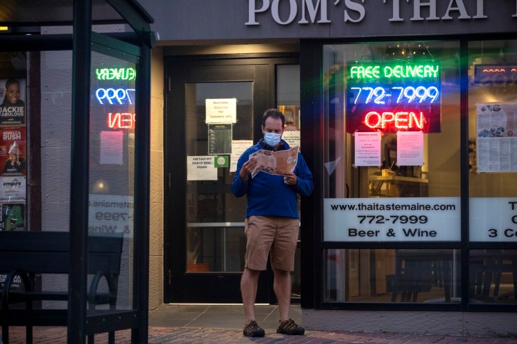 A person peruses a take-out menu outside of a restaurant on Congress Street in downtown Portland on August 31.