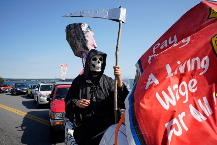 PORTLAND, ME - SEPTEMBER 7: Dressed as the Grim Reaper, Asher Platts, a volunteer with the Southern Maine Workers' Center, stands in the back of a truck as a caravan leaves the Eastern Prom in Portland on Monday, September 7, 2020. The caravan was organized by the Southern Maine Workers' Center and the Southern Maine Labor Council to draw attention to the need for legislation to protect workers, reinstate unemployment benefits, support the U.S. Postal Service and to address economic and health racial disparities. Organizers dubbed the caravan a funeral procession due to the number of workers who have died of COVID-19. (Staff Photo by Gregory Rec/Staff Photographer)