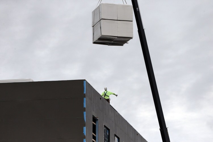 A worker makes hand signals to a crane operator lowering materials onto the roof of a building under construction at the corner of Commercial and Center streets in Portland on Sept. 2. Construction has been one of the remaining bright spots in Maine's struggling economy.