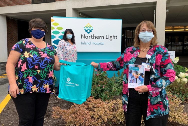 From left, Joanne Booth, Sodexo senior manager; Bridgette Gemelli, community health navigator; and Terri Vieira, president of Inland Hospital, hold an emergency food bag and a Food Resource Guide.