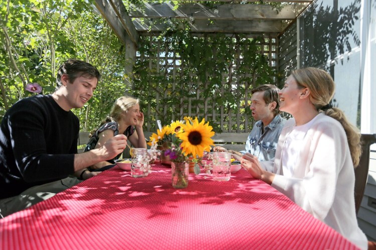 Portland housemates Eoghan Sweeney, left, Kat McNeil, Andrew Tufts and Anna Ackerman, all of whom work remotely at least in part, prepare to eat lunch together on their back deck. Sharing a mid-day meal, getting to hear "snippets" of each other's days, has been a pleasure of working from home, said Ackerman. 