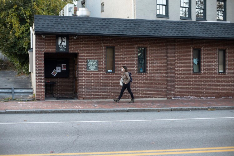 A woman walks past the Flask Lounge on Spring Street in Portland on Tuesday. Bars in Maine will be allowe to reopen next month under the governor's plan.