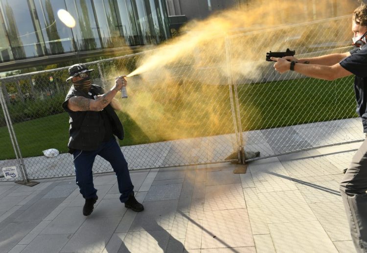 A man sprays Mace, left, at a security guard on Saturday in Denver. A private security guard working for a TV station was in custody Saturday after a person died from a shooting that took place during dueling protests in downtown Denver, the Denver Post reported.
