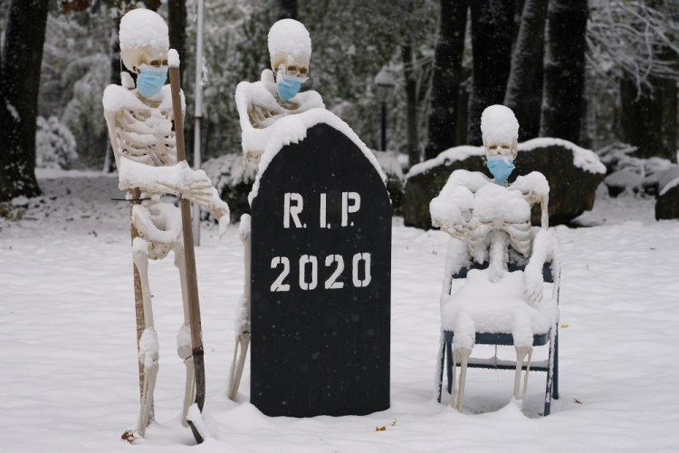Snow falls on masked skeletons ready to bury the year 2020 on Friday in North Andover, Mass. 

