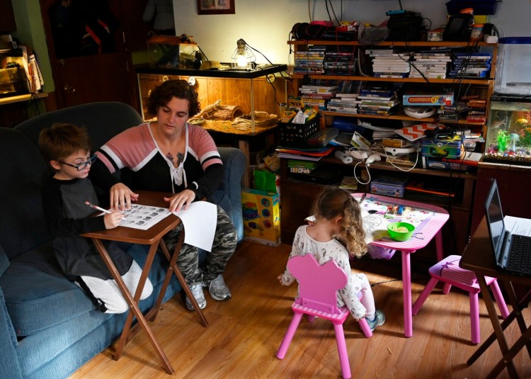 Ashley Whitman helps her son Blake with his homework as her daughter Bella colors at their Winslow home on Thursday.  Whitman had her hours as a preschool teacher cut back, and she can't find a job that fits her schedule as she cares for her three children during the coronavirus pandemic.