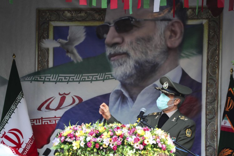 In this photo released by the official website of the Iranian Defense Ministry, Defense Minister Gen. Amir Hatami speaks during a funeral ceremony for Mohsen Fakhrizadeh, a scientist who was killed on Friday, shown in the banner at background, in Tehran, Iran, Monday, Nov. 30, 2020. Iran held the funeral Monday for the slain scientist who founded its military nuclear program two decades ago, with the Islamic Republic's defense minister vowing to continue the man's work "with more speed and more power." (Iranian Defense Ministry via AP)