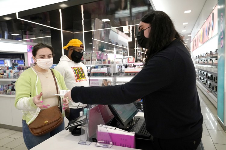 Druhan Parker, right, works behind a plexiglass shield Thursday, as he checks out shoppers Cassie Howard, left, and Paris Black in Chicago. 
