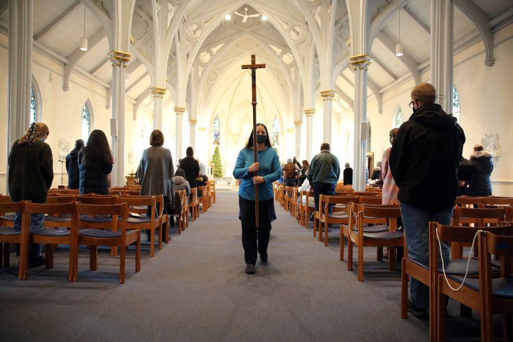 Churchgoers are socially distanced at Cathedral of the Immaculate Conception in Portland as church sacristan Dianne Tardy carries the cross at the end of daily Mass on Wednesday. 