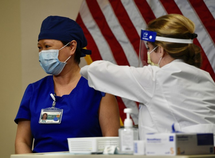 Nurse Song Lee looks away as she gets a dose of the Pfizer-BioNTech COVID-19 vaccine from nurse practitioner Christie Aiello at Providence St. Joseph Hospital in Orange, Calif., Wednesday, Dec. 16, 2020. (Jeff Gritchen/The Orange County Register via AP)