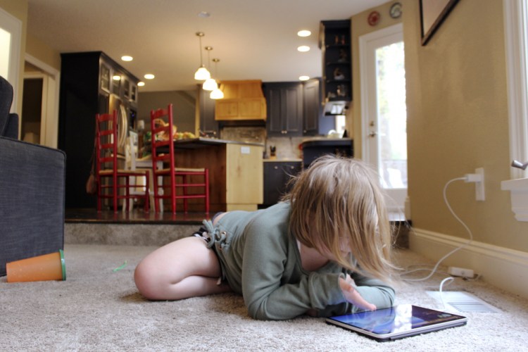 Lizzie Dale sprawls on the floor to play games on an iPad as her siblings work on school work in the kitchen behind her in their home in Lake Oswego, Ore., on Oct. 30. In Oregon, one of only a handful of states that has required a partial or statewide closure of schools in the midst of the COVID-19 pandemic, parents in favor of their children returning to in-person learning have voiced their concerns and grievances using social media, petitions, letters to state officials, emotional testimonies at virtual school board meetings and on the steps of the state's Capitol.

