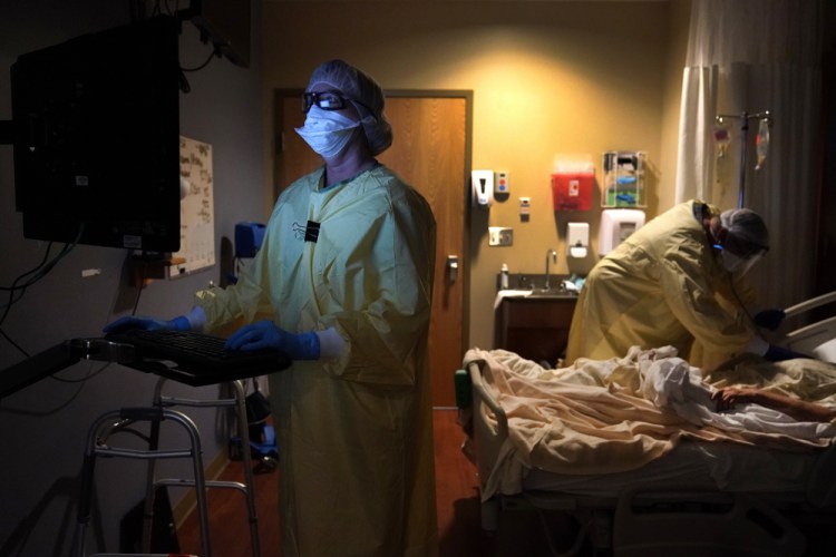 Registered nurse Shelly Girardin, left, is illuminated by the glow of a computer monitor as Dr. Shane Wilson examines a COVID-19 patient at Scotland County Hospital in Memphis, Mo., last month. 