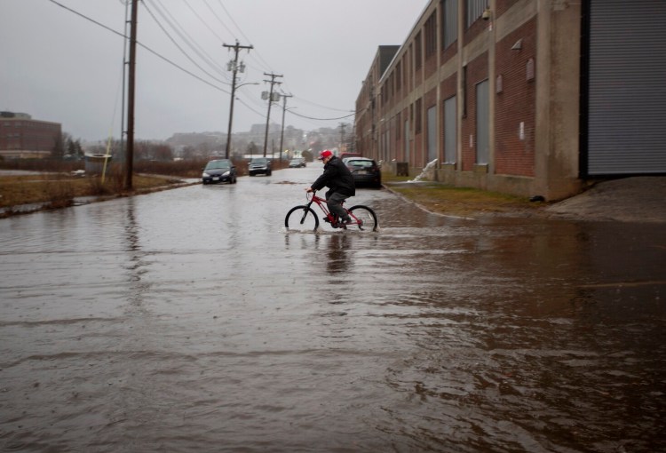 A man rides a bicycle through a flooded section of Elm Street in Portland on Saturday. Heavy rain and winds soaked southern and coastal Maine while some inland areas got more than a foot of snow.
