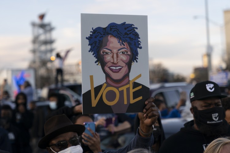 People in the crowd hold up an image of Stacey Abrams as President-elect Joe Biden speaks in Atlanta, Monday to campaign for Georgia Democratic candidates for U.S. Senate, Rev. Raphael Warnock and Jon Ossoff.