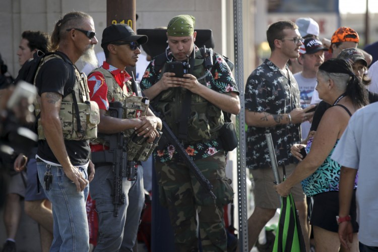 Gun-carrying men wearing Hawaiian print shirts associated with the boogaloo movement watch a demonstration near where President Trump had a campaign rally in Tulsa, Okla., in June. The anti-government promotes violence and a second U.S. civil war.

